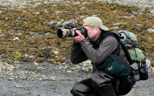 Man pointing camera at something out of frame while wearing hiking gear.
