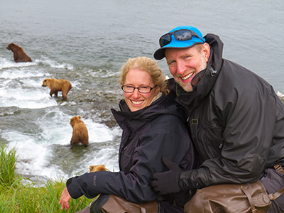 Couple posing in front of a group of bears playing in the water
